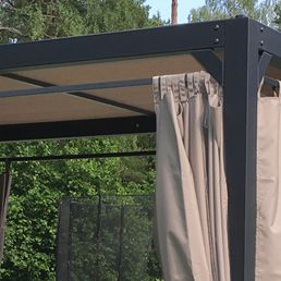 Solskydd för gunga med svart ram och sidogardiner i beige färg.