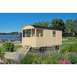 A two-wheeled cart shaped like a house, beige in color, placed in a natural setting near a body of water.
