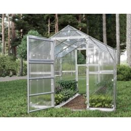 Ett litet växthus av glas i en naturlig omgivning, med genomskinliga väggar och takluckor.