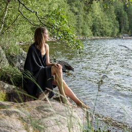 Vaaleanharmaa 90x180 cm saunapyyhe, jota henkilö kantaa joen rannalla kauniissa luonnonpaikassa.