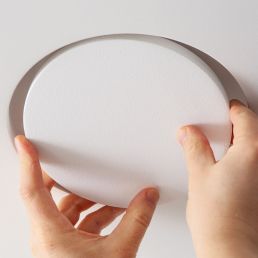 Kaks kätt paigaldavad ümmarguse valge ventilatsiooni plafondi siledale pinnale.