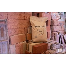 Kraftpapperspåse med tryckt logotyp 'Ahjusegu 0-2mm' placerad mot en tegelstensbakgrund.