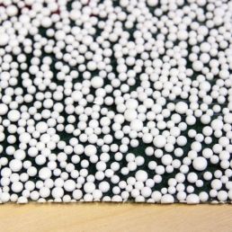 Fotol on Tuplex alusmaterjal, mida kasutatakse põrandakatete all. Näha on väikesed valged polüstüreenhelmed rohelisel taustal.