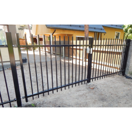 Svart metallgrind för bilinfart med vertikala spjälor, bakgrund av ett gult hus.