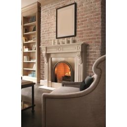 Dekoratiivne telliskivist kamin, sokkel ja raamitud tühi pildiraam, helehall tugitool esiplaanil.