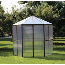 Ett sexkantigt växthus med vita metallramar och genomskinliga paneler, placerat på gräs i en grön miljö.