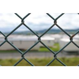 A metal fence covered with gray PVC, sharply focused in the foreground, with a blurred view of an airport in the background.