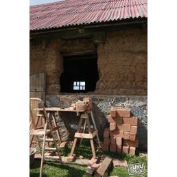 25 kg fyllmedel för renovering av lerhus, förpackat i pappkartonger och staplat intill en gammal lervägg samt en metallställning.