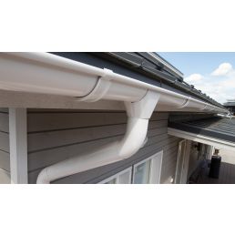 Valkoinen metallinen sadevesikouru ja syöksytorvi on asennettu talon katon reunaan, näkyvillä olevat kiinnikkeet.